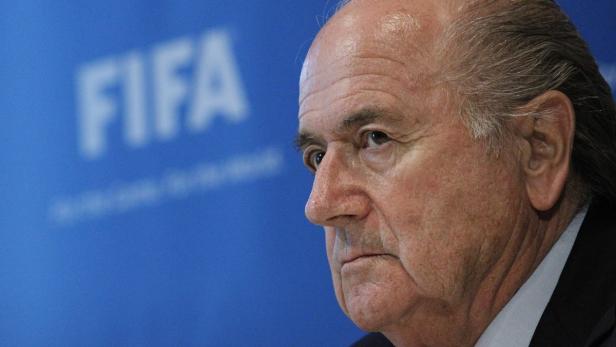 Sepp Blatter vor einem blauen Hintergrund mit dem FIFA-Logo.