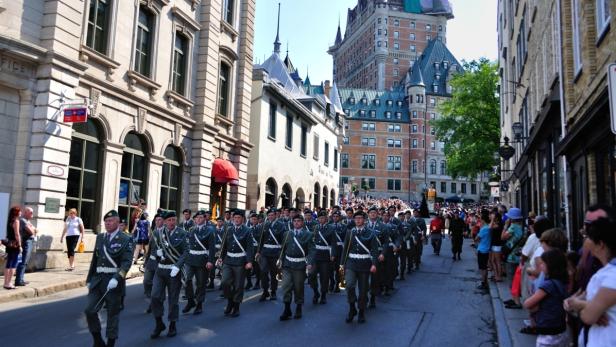 Eine Militärparade zieht durch eine Straße in Québec vor dem Fairmont Le Château Frontenac.