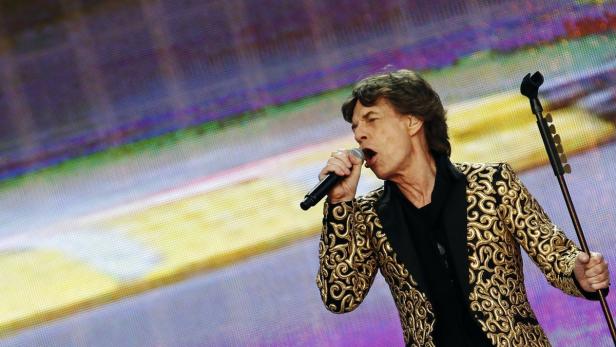 Mick Jagger singt mit einem Mikrofon in der Hand auf der Bühne.