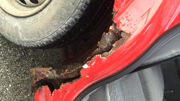Ein rotes Auto mit starkem Rostbefall an der Karosserie.