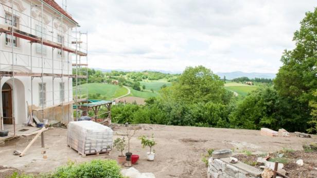 Ein Haus mit Baugerüst vor einer grünen Hügellandschaft.