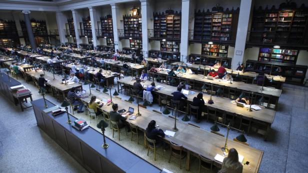 Eine große Bibliothek mit vielen Menschen, die an langen Tischen sitzen und lernen.