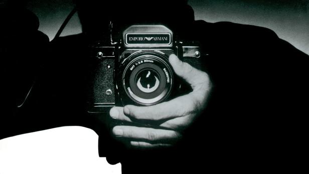 Eine Person hält eine analoge Kamera der Marke Emporio Armani.