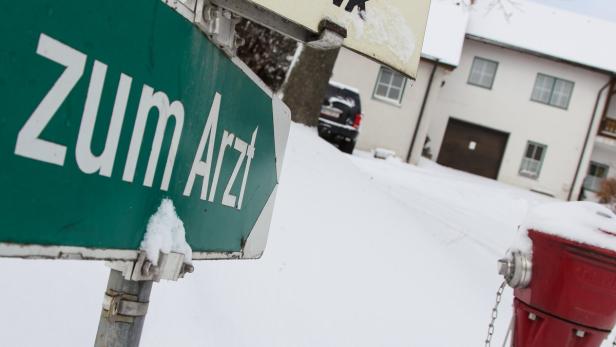 Ein grünes Schild mit der Aufschrift „Zum Arzt“ im verschneiten Winter.