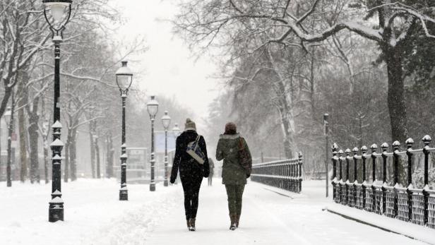 Zwei Frauen gehen einen verschneiten Parkweg entlang.