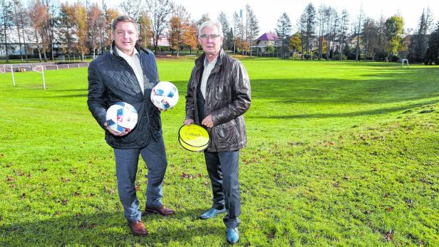 Zwei Männer stehen auf einem Fußballfeld, einer hält zwei Bälle, der andere eine gelbe Scheibe.