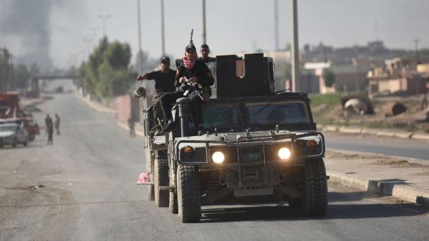 Bewaffnete Männer fahren in einem Militärfahrzeug eine Straße entlang.