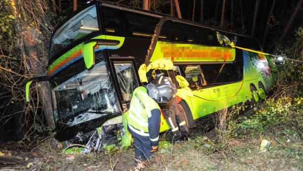 Ein verunglückter, grüner Reisebus ist gegen einen Baum gefahren; Rettungskräfte sind vor Ort.