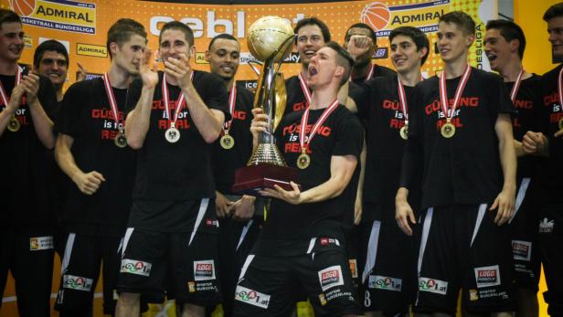 Ein Basketballteam feiert mit dem Pokal in der Hand ihren Sieg.