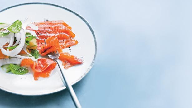 Ein Teller mit Lachsscheiben, Kokosraspeln und Minze wird mit einer Gabel angerichtet.