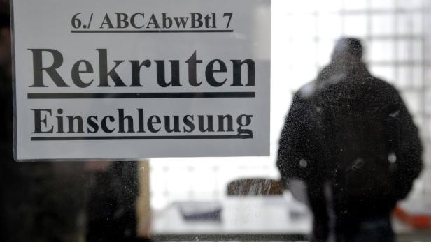 Ein Schild mit der Aufschrift „Rekruten Einschleusung“ hängt an einer Tür, hinter der eine Person steht.