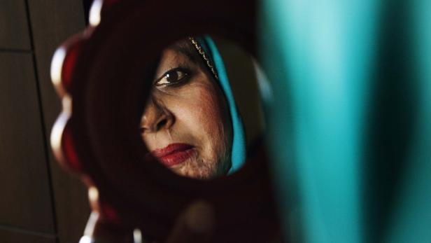 Eine Frau mit Kopftuch blickt in einen Handspiegel.