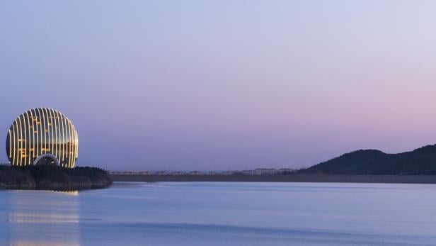 Das Sheraton Huzhou Hot Spring Resort am Ufer eines Sees bei Dämmerung.