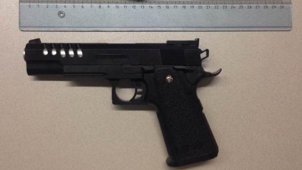 Eine schwarze Pistole liegt auf einem Tisch neben einem Lineal.