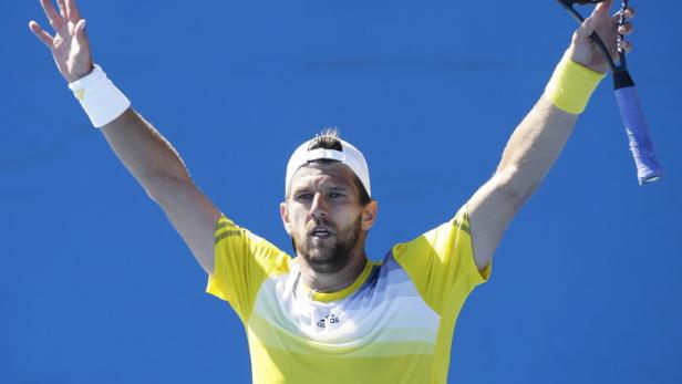 Ein Tennisspieler mit gelbem Hemd und weißer Kappe jubelt mit erhobenen Armen.