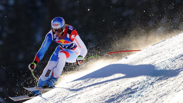 Ein Skirennfahrer in blau-weisser Rennkleidung fährt eine schneebedeckte Piste hinunter.