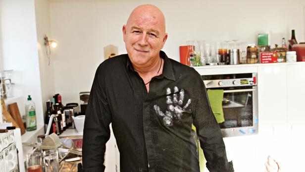 Ein Mann mit einem schwarzen Hemd mit Handabdruck steht in einer Küche.