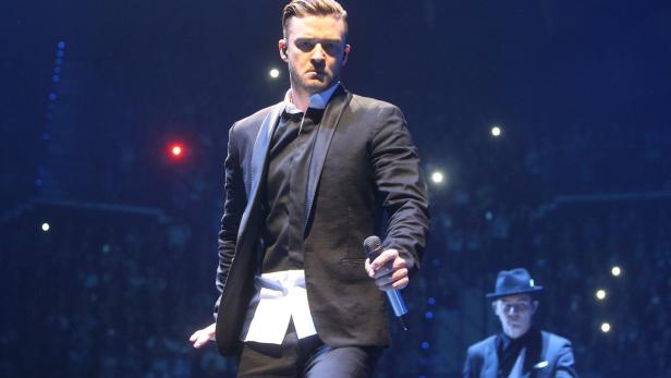 Justin Timberlake tritt in einem schwarzen Anzug auf einer Bühne auf.