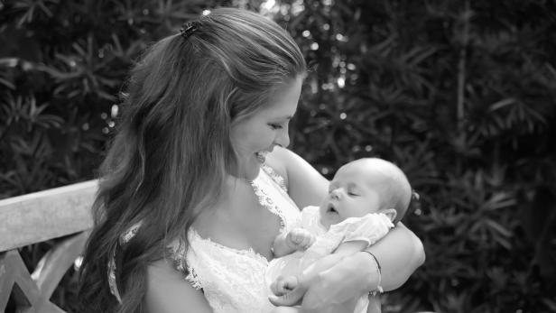 Eine lächelnde Mutter hält ihr schlafendes Baby im Arm.