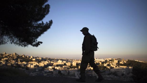 Ein Soldat mit Rucksack geht vor einer Stadt im Gegenlicht.