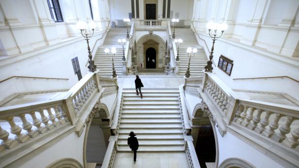 Zwei Personen steigen eine große, weiße Treppe in einem Gebäude hinauf.