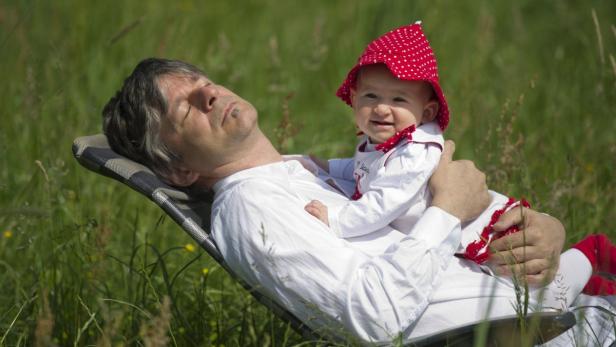 Ein Mann ruht sich mit einem kleinen Kind auf einer Liege im Grünen aus.