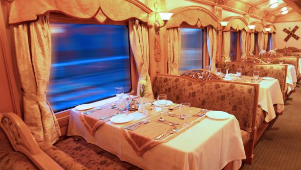 Ein Speisewagen mit gedeckten Tischen und Blick aus dem Fenster.