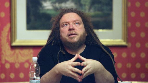 Ein Mann mit Dreadlocks sitzt an einem Tisch und blickt nach oben.