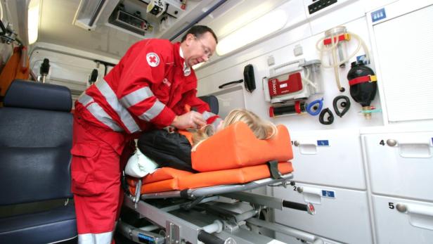 Ein Sanitäter in roter Uniform behandelt eine Patientin auf einer Liege im Krankenwagen.