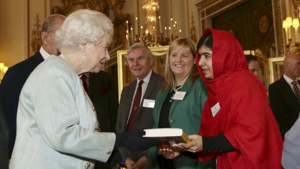 Königin Elisabeth II. empfängt Malala Yousafzai, die ihr ein Buch überreicht.