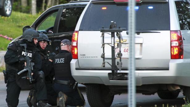 Polizisten mit Schutzwesten und Helmen knien hinter einem silbernen SUV.
