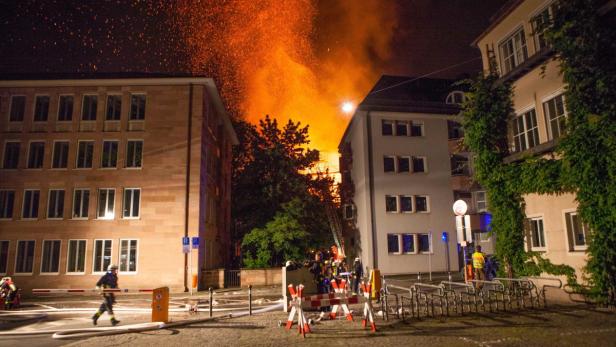 Ein Brand zwischen Gebäuden, mit Feuerwehrleuten im Einsatz.