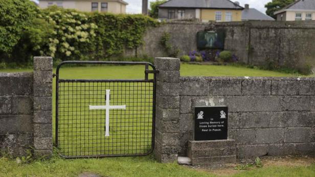 Ein Friedhofstor mit einem weißen Kreuz vor einer Steinmauer.
