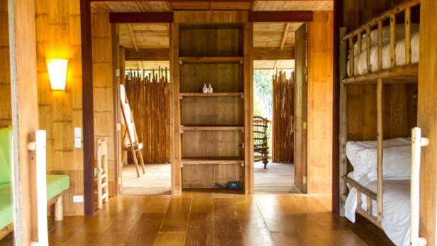 Innenansicht eines Zimmers mit Holzboden, Bambuswänden und einem Etagenbett.