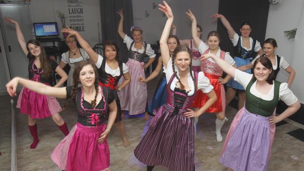 Eine Gruppe junger Frauen in Dirndln tanzt in einem Raum.