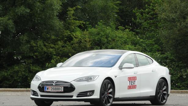 Ein weißes Tesla Model S vor einer grünen Baumreihe.