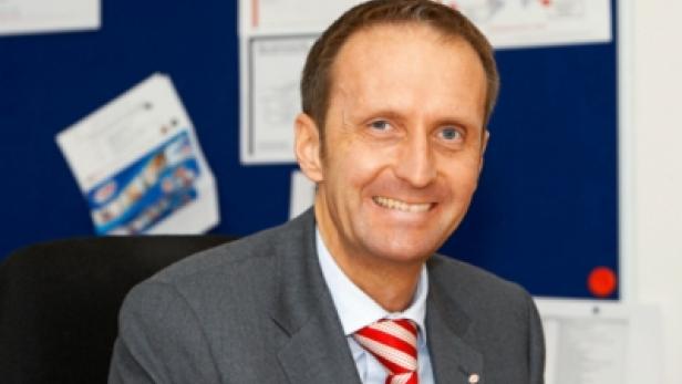Ein lächelnder Mann im Anzug mit rot-weiß gestreifter Krawatte.