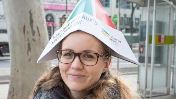 Eine Frau mit Brille trägt einen Papierhut mit der Aufschrift „Hau den Hut auf's Miete zahlen!“.