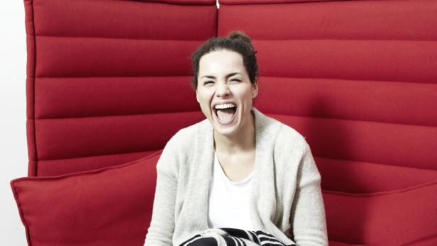 Eine lachende Frau sitzt auf einem roten Sofa.