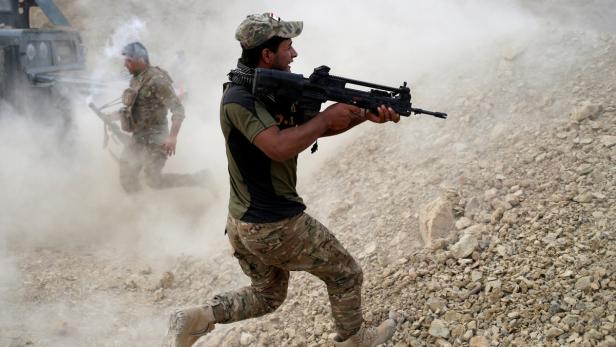 Zwei Soldaten rennen mit Gewehren durch eine staubige, felsige Landschaft.