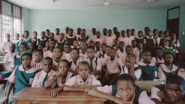 Eine Schulklasse mit vielen dunkelhäutigen Kindern in Uniformen sitzt in einem Klassenzimmer.