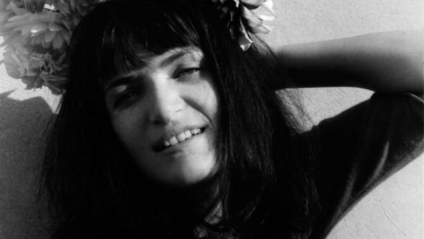 Eine Frau mit dunklen Haaren und einem Blumenkranz posiert vor einer Wand.