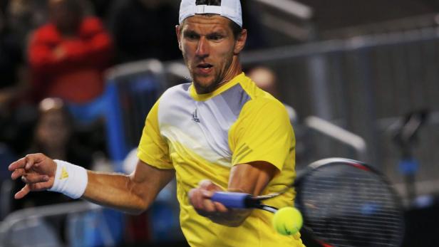 Ein Tennisspieler in gelbem Hemd schlägt einen Ball.