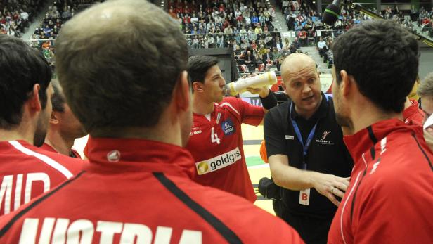Ein Handballtrainer bespricht sich mit seiner Mannschaft, während ein Spieler trinkt.