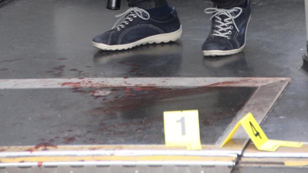Blutspuren und Beweismarkierungen an einem Tatort, mit Schuhen im Hintergrund.
