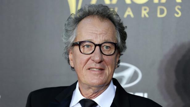 Geoffrey Rush posiert auf einem roten Teppich.