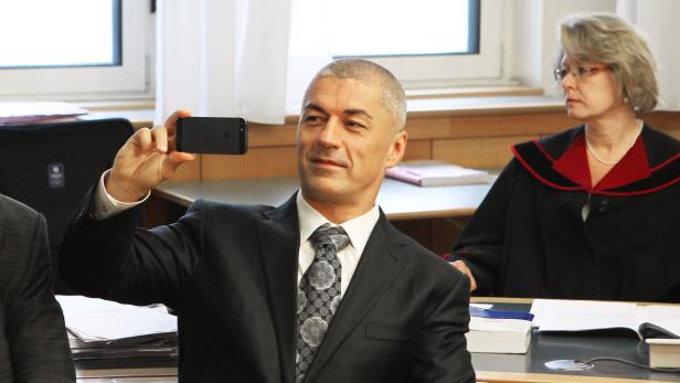 Ein Mann im Anzug macht ein Foto mit seinem Smartphone, während eine Frau im Hintergrund sitzt.