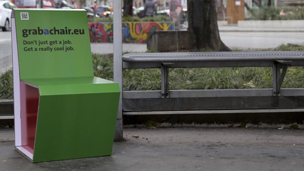 Ein grüner Pappstuhl mit der Aufschrift grabachair.eu steht an einer Bushaltestelle.