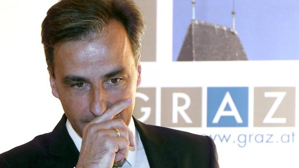 Ein Mann mit Anzug hält seine Hand vor das Gesicht, im Hintergrund steht „Graz“.