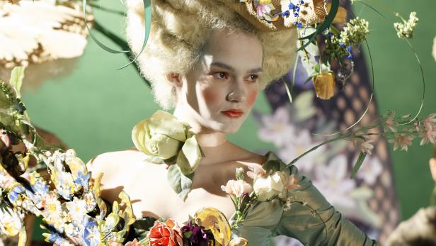 Eine Frau in einem historischen Kleid und einem aufwendigen Hut mit Blumen und Federn.